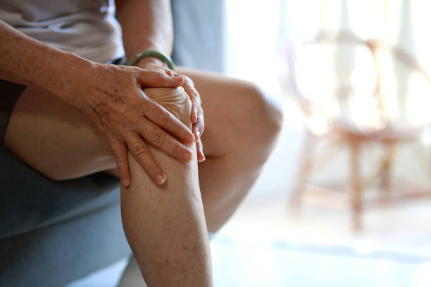 An elderly man holds his knee in discomfort from a chronic condition.