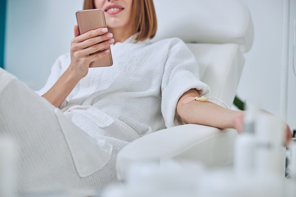 woman receiving iv therapy while on her phone scrolling and relaxing